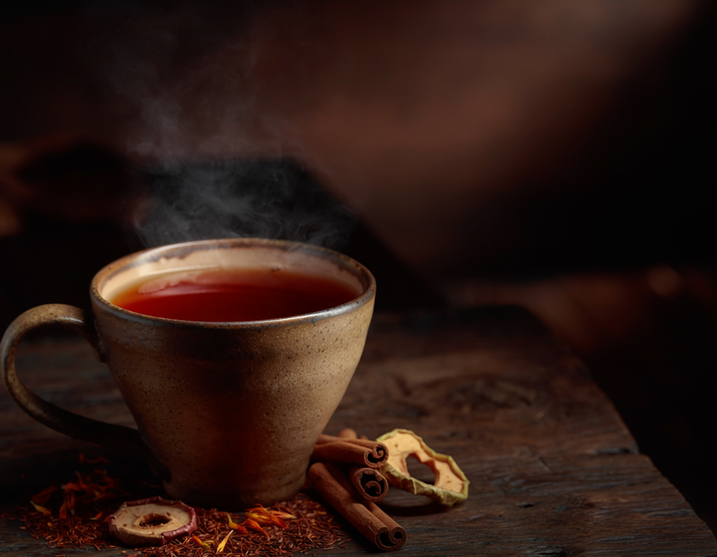 Steaming cup of tea on a wooden surface with cinnamon sticks and dried fruits.