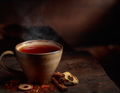 Steaming cup of tea on a wooden surface with cinnamon sticks and dried fruits.