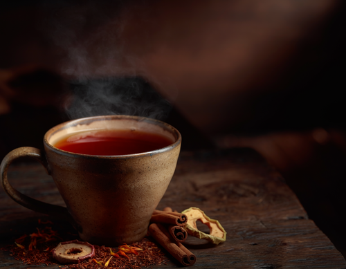 Steaming cup of tea on a wooden surface with cinnamon sticks and dried fruits.