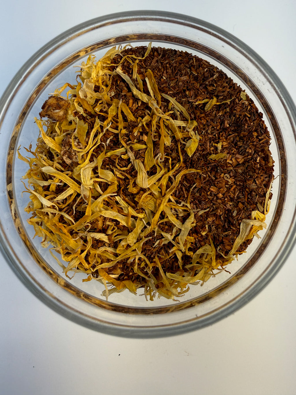 Glass jar with yellow and brown dried herbs on a white background