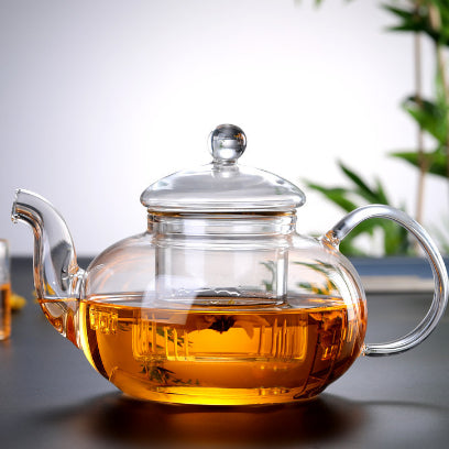 Clear glass teapot with a lid filled with tea on a dark surface.